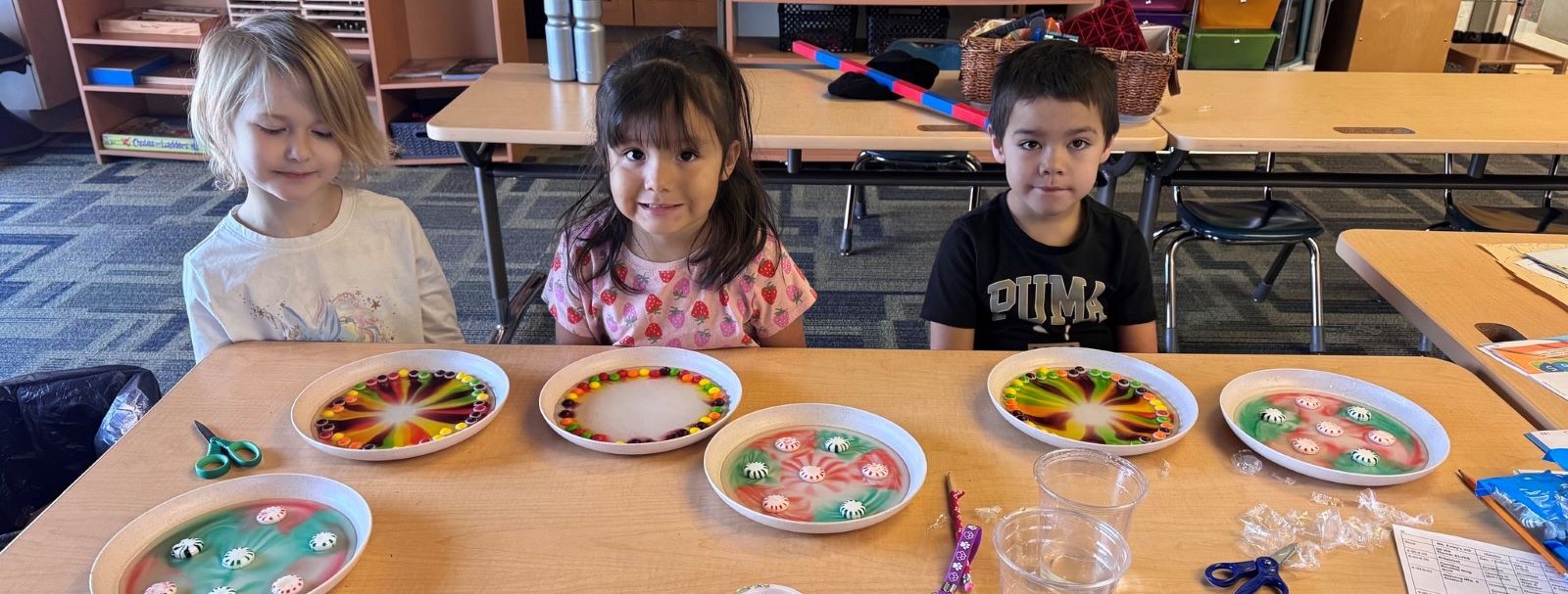 Students creating art made from different colored candy on plates.
