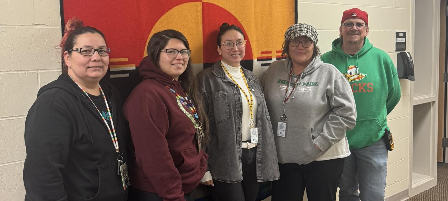 School staff members standing in front of a banner in the school hall.