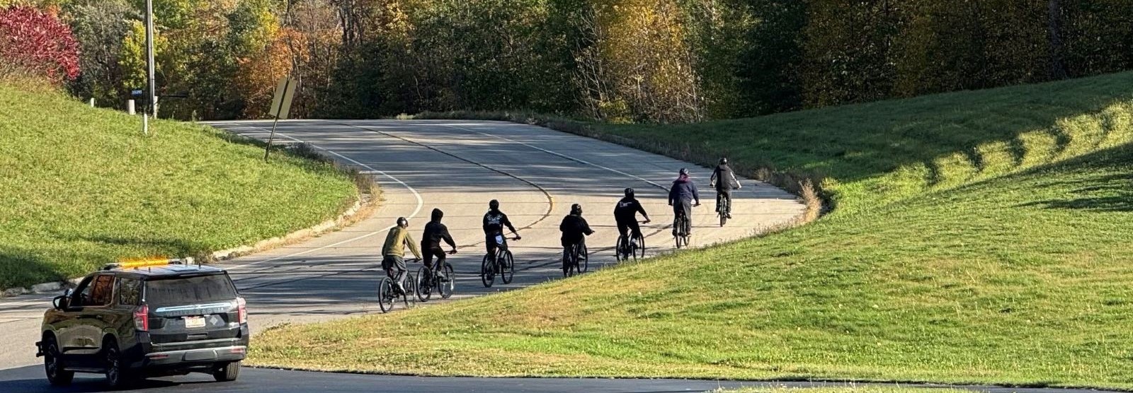 Several students riding bicycles along a road, surrounded by greenery and blue skies.